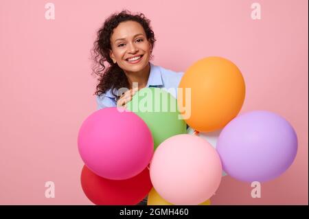 Gros plan, portrait en face de la magnifique femme afro-américaine aux cheveux mausseux souriant avec un sourire éclatant debout derrière des ballons d'air colorés isol Banque D'Images