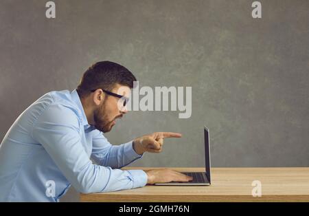 Vue latérale d'un homme choqué assis sur un bureau et regardant un ordinateur portable pointant vers l'écran Banque D'Images