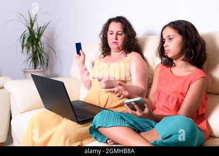 Mère et fille, assis sur un canapé, choisissant ce qu'ils vont acheter en ligne avec leur ordinateur portable, tout en le comparant avec ce qu'ils ont cherché o Banque D'Images