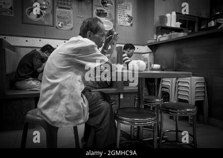 Un vieil homme attend sa nourriture dans un restaurant à Yuen long, New Territories, Hong Kong (version monochrome) Banque D'Images