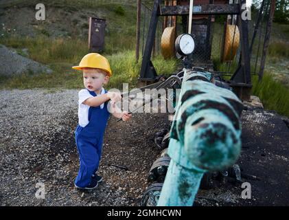 Adorable enfant dans un casque de construction à l'aide d'une clé industrielle lors de la réparation d'un tuyau de vérin de pompe de puits d'huile. Boulon de serrage de l'ouvrier d'huile mignon sur le tuyau. Concept de l'industrie pétrolière et de l'enfance. Banque D'Images