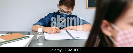 Garçon avec masque de visage écrivant à l'école Banque D'Images