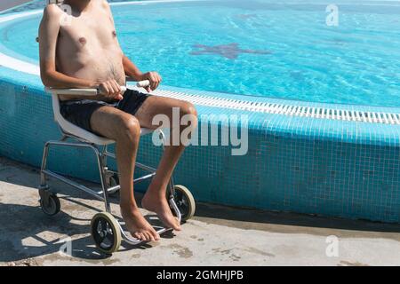 Homme handicapé à la piscine ascenseur pour fauteuil roulant et transféré dans l'eau par un assistant. Banque D'Images