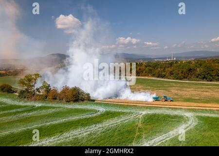 Vue aérienne d'un tracteur qui répand de la chaux sur les champs agricoles pour améliorer la qualité du sol après la récolte d'automne. L'utilisation de poudre de chaux pour neutraliser Banque D'Images