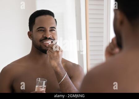 Beau homme africain tenant un verre d'eau et prend des pilules Banque D'Images