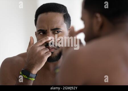 Un homme africain regarde dans le visage de contact de miroir serre le bouton Banque D'Images