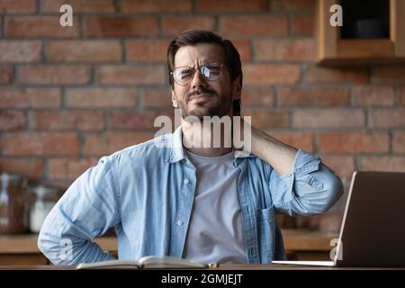Homme fatigué dans les lunettes frottant les muscles raides du cou, sensation de douleur Banque D'Images