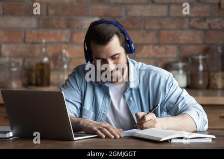 Gros plan homme dans un casque prenant des notes, à l'aide d'un ordinateur portable Banque D'Images