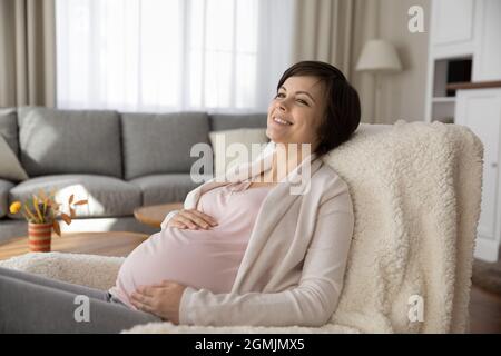 Charmante femme enceinte détendez-vous dans une chaise confortable dans le salon Banque D'Images