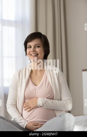 Bonne femme enceinte millénaire s'asseoir sur le coup de lit grand ventre Banque D'Images