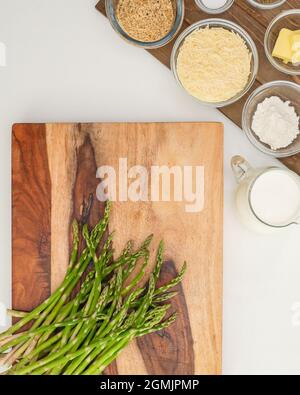Asperges vertes sur une planche à découper en bois, et quelques ingrédients sur une table de cuisine. Recette de cocotte d'asperges. Banque D'Images