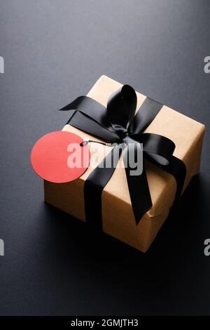 Boîte-cadeau avec noeud noir et étiquette de prix rouge sur fond noir. Banque D'Images