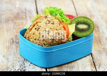 Boîte à lunch saine contenant un rouleau de fromage à grains entiers avec de la laitue, de la tomate et des kiwis Banque D'Images