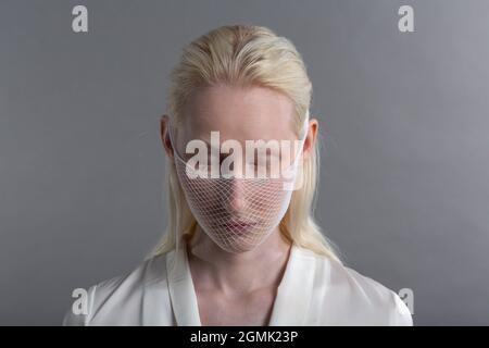 Gros plan portrait de blanc blanc albino blonde femme modèle de mode port quarantaine médical masque facial filet grossier sur fond gris. Couverture de visage Banque D'Images