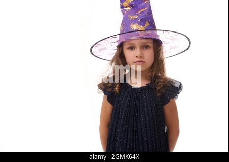 Portrait d'une magnifique petite fille confiante portant un chapeau de génie et vêtue d'une robe de carnaval élégante, regardant la caméra posant avec des bras croisés agai Banque D'Images