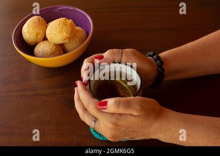 Les femmes tiennent une tasse de thé, et un bol de petits pains de fromage sur le côté. Banque D'Images