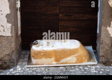 Vieux bain de métal lyes à l'envers sur le pavé de pavés à l'extérieur devant la grande porte en bois. Élimination des déchets de grande taille. Composition vintage Banque D'Images