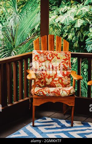 Une photo verticale d'une chaise en bois avec des coussins à motifs colorés sur une terrasse Banque D'Images