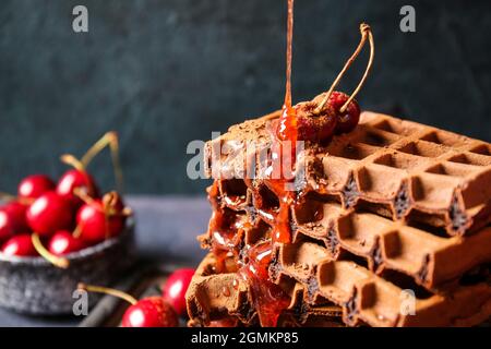 Verser la garniture sur de délicieuses gaufres belges au chocolat avec de la cerise sur fond noir, gros plan Banque D'Images