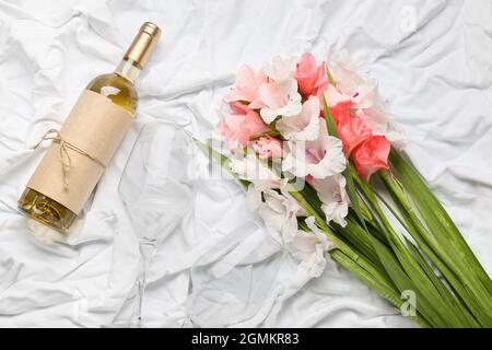 Magnifiques fleurs gladiolus, bouteille de vin et verre sur fond de tissu léger Banque D'Images