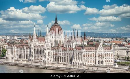 Vue d'été du Parlement hongrois construit dans le style néo-gothique le long du Danube avec une parfaite symétrie avec ciel bleu nuageux Banque D'Images