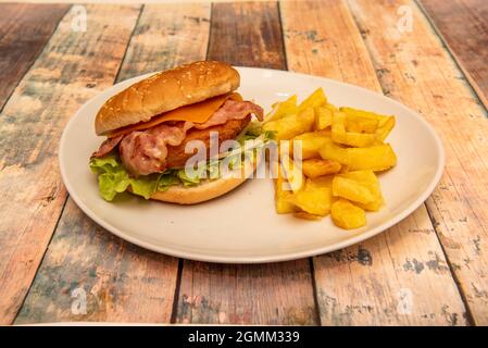 Hamburger au poulet croustillant avec laitue Iceberg, oignon blanc cru, bacon fumé frit, cheddar et frites maison Banque D'Images