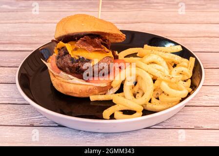 Hamburger au bœuf avec fromage cheddar, jambon ibérique frit, tomates et laitue avec frites en tranches spiralées Banque D'Images