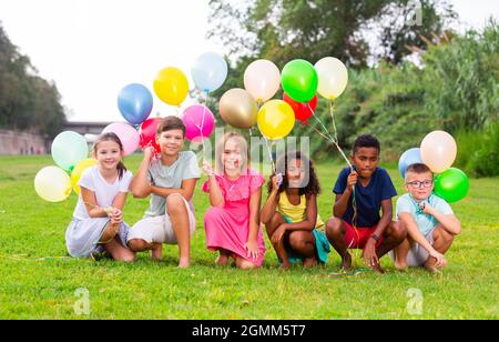 Joyeux préadolescents garçons et filles avec des ballons colorés sur la pelouse verte Banque D'Images
