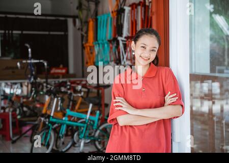 une femme portant un t-shirt à col rouge avec des bras pliés se tient devant une cabine de vélo Banque D'Images