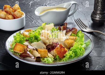 Salade César au poulet avec sauce classique, croûtons et poivre, sur fond noir Banque D'Images