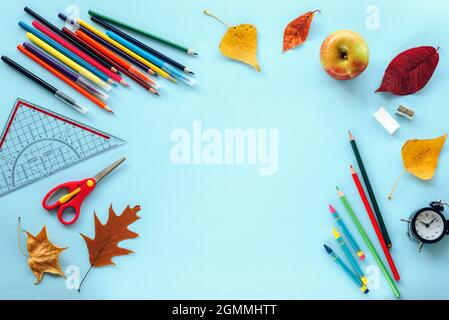 Fournitures scolaires papeterie, crayons de couleur, ciseaux, règle, réveil, pomme, feuilles d'automne sur fond bleu. Concept de retour à l'école. Vue de dessus Banque D'Images