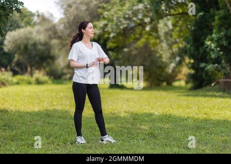 Une jeune femme en vêtements de sport ouvre une bouteille d'eau potable. En arrière-plan, un parc vert ensoleillé. Repos après l'entraînement. Banque D'Images