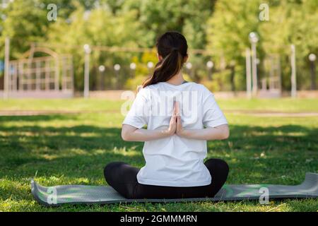 Yoga. Une jeune femme en vêtements de sport, assise fait un exercice, faisant du yoga dans le parc sur l'herbe. Vue arrière. Copier l'espace. Concept d'un sain Banque D'Images