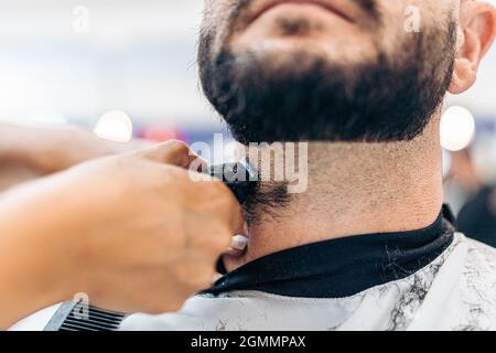 Vue rapprochée d'une main rasant une barbe avec un rasoir électrique dans un salon Banque D'Images