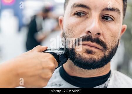 Vue rapprochée d'un coiffeur rasage d'une barbe avec un rasoir électrique dans un salon Banque D'Images