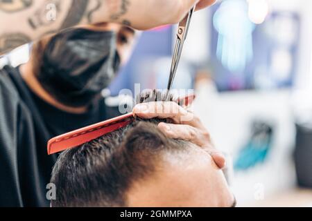 Coiffeur avec masque coupant les cheveux d'un client dans un salon de coiffure Banque D'Images