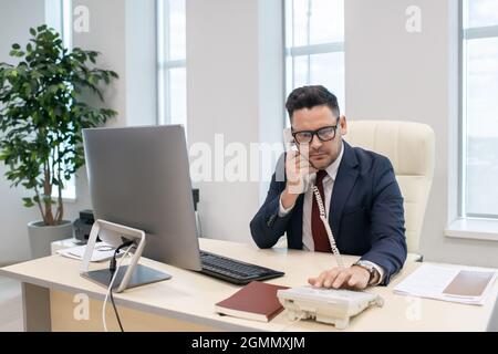 Homme d'affaires ou directeur d'entreprise en composant le numéro de téléphone de son lieu de travail au bureau Banque D'Images