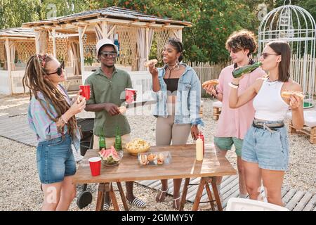 Jeunes amis ayant des hot dogs et des boissons à l'extérieur tout en appréciant le week-end d'été Banque D'Images