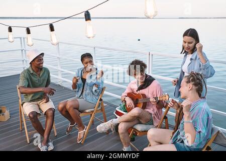 Les jeunes hommes et femmes qui chantent à la guitare tout en passant du temps sur la jetée le jour d'été Banque D'Images