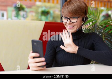 Jeune femme d'affaires souriante lors d'un appel vidéo en ligne. Réunion en ligne avec des amis - elle souriant et agitant la main et disant Bonjour. Banque D'Images
