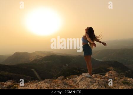 Bonne femme célébrant le succès en respirant et en hurlant les bras qui s'étirent au coucher du soleil Banque D'Images