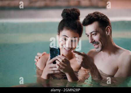 Portrait d'un jeune couple dans une piscine thermale de source chaude intérieure, en prenant le selfie. Banque D'Images