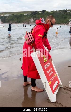 Un sauveteur RNLI déplace un panneau d'avertissement le long de Bantham Beach, Devon. Banque D'Images