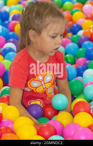 Petite fille caucasienne de cinq ans regardant de côté parmi les boules multicolores dans le centre de jeu à l'intérieur Banque D'Images