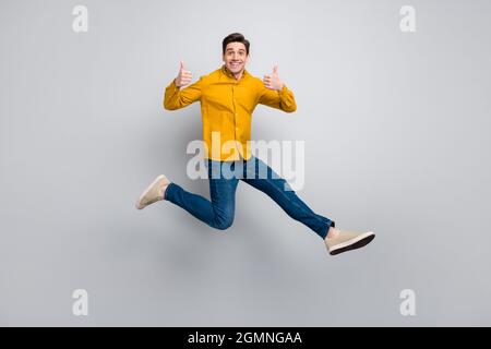 Vue sur toute la longueur du corps de l'homme gai attrayant saut montrant le humbup isolé sur fond gris couleur Banque D'Images