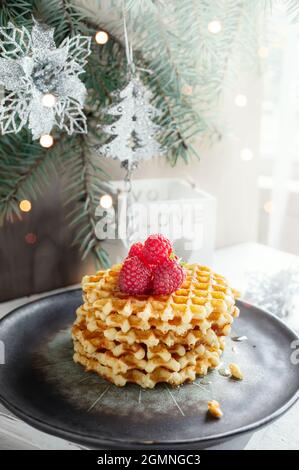 Gaufres rondes avec framboises sur la table de Noël. Pâtisseries festives sur le fond d'un arbre de Noël. Banque D'Images