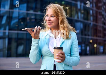Femme d'affaires tient une tasse de papier de café dans ses mains et parle au téléphone. Banque D'Images