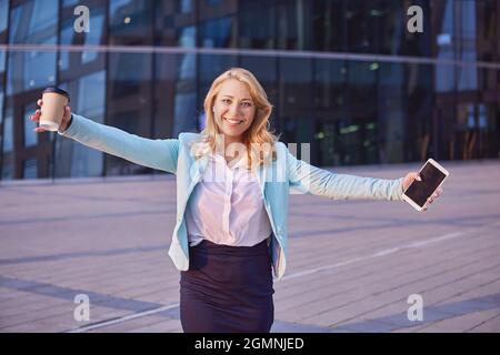 Une femme joyeuse en costume d'affaires a fait passer les mains dans lesquelles le café et le smartphone. Banque D'Images