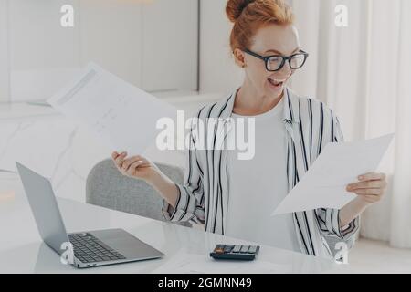 Une jeune femme positive aux cheveux rouges calcule les charges d'utilité engagées dans la planification du budget mensuel Banque D'Images