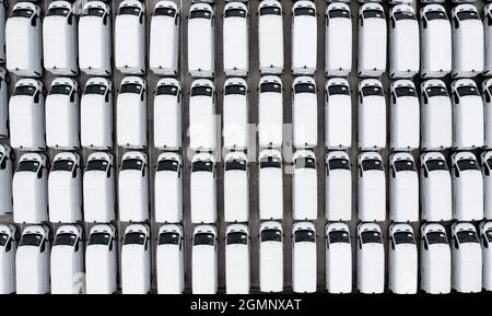 Une vue aérienne des rangées de camionnettes blanches nouvellement fabriquées sur un quai commercial avant l'expédition pour l'exportation ou la logistique d'importation Banque D'Images